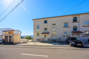 Un immeuble à plusieurs étages, avec un espace de stationnement à l’avant, où une voiture noire est garée sur l’une des places disponibles.