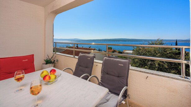 Un balcon avec une table et des chaises, un panier de fruits et deux verres de vin.