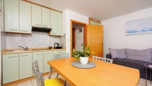 Une cuisine avec des meubles de couleur vert clair, une table à manger en bois avec deux chaises, et une plante en pot posée sur la table.