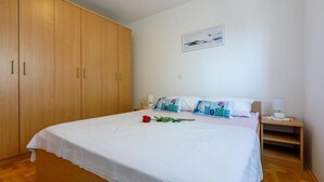 A bedroom with a large wooden wardrobe, a bed with white bedding, a single red rose, and a wall-mounted picture. - Apartments Pirin (Crikvenica)