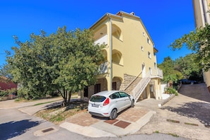 A white car parked in front of a yellow building with a staircase leading to an upper level. - Apartments Pirin (Crikvenica)