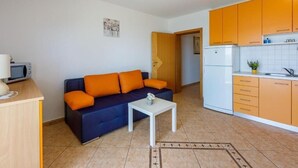A compact living space with a sofa, a small table, a kitchenette, and a door leading to another room. - Apartments Pirin (Crikvenica)