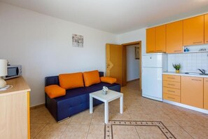 A compact living space with a sofa, a small table, a kitchenette, and a door leading to another room. - Apartments Pirin (Crikvenica)