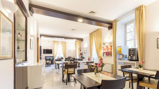 Une salle à manger d’hôtel avec plusieurs tables et chaises, un coin cuisine et un téléviseur fixé au mur.
