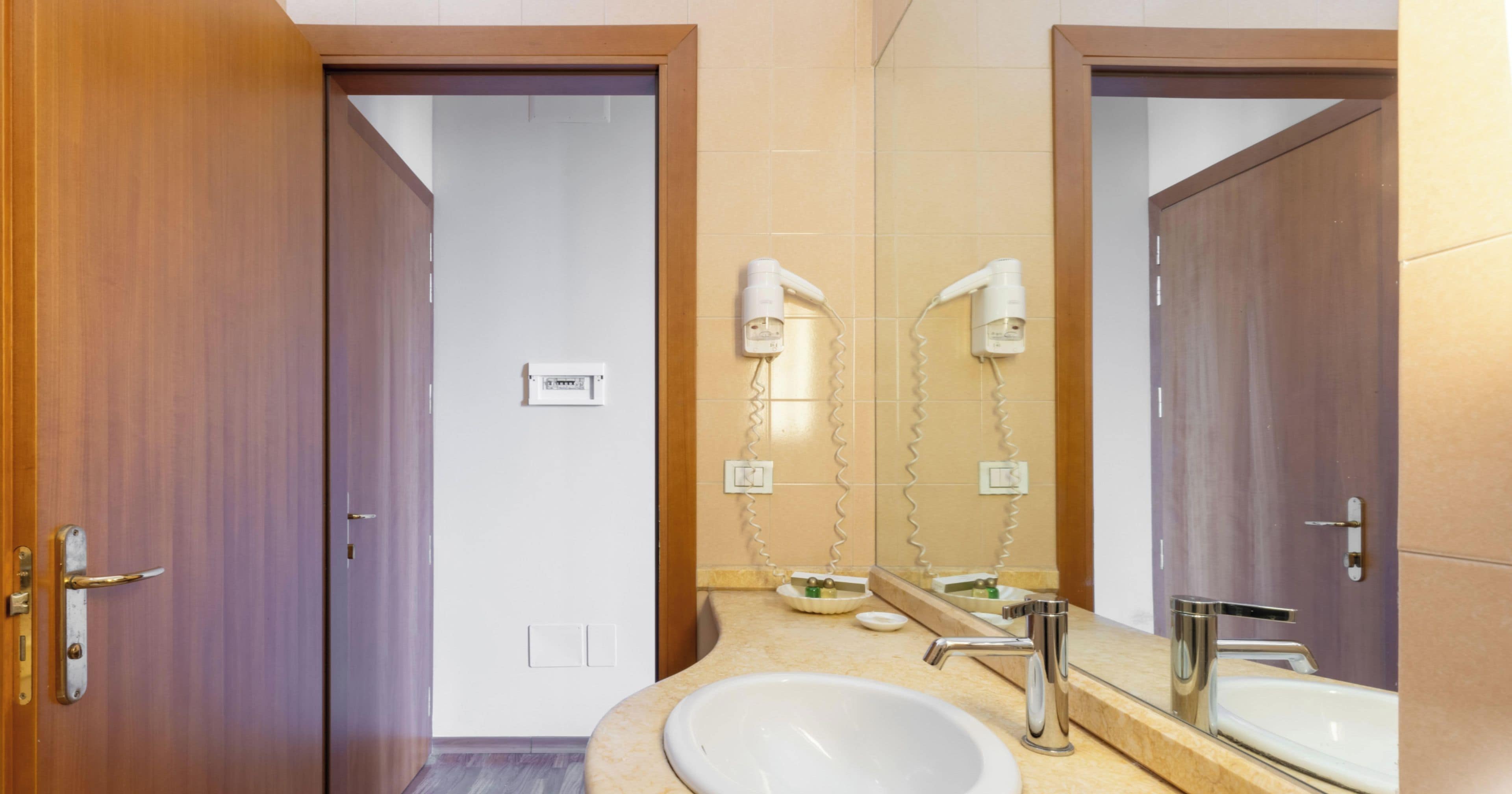 A bathroom with two sinks, a mirror, and a hairdryer mounted on the wall.