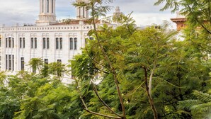 Un bâtiment historique doté d’une tour imposante et de fenêtres en arc de cercle, entouré d’arbres verdoyants.