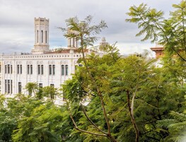 Un edificio con una torre imponente e ampie finestre, circondato da alberi rigogliosi.