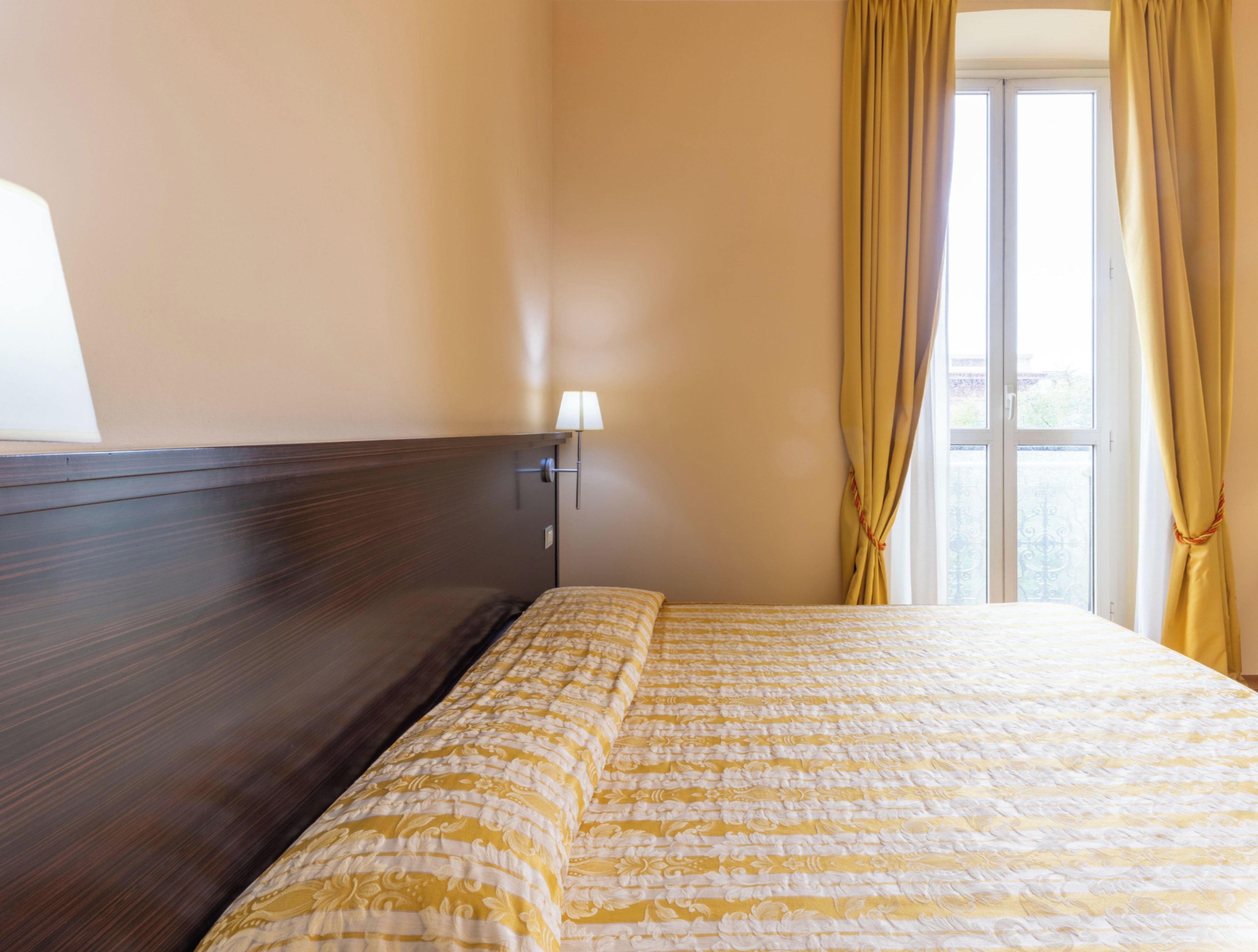 Une chambre d’hôtel avec un lit, une table de chevet, une lampe et une fenêtre avec des rideaux.