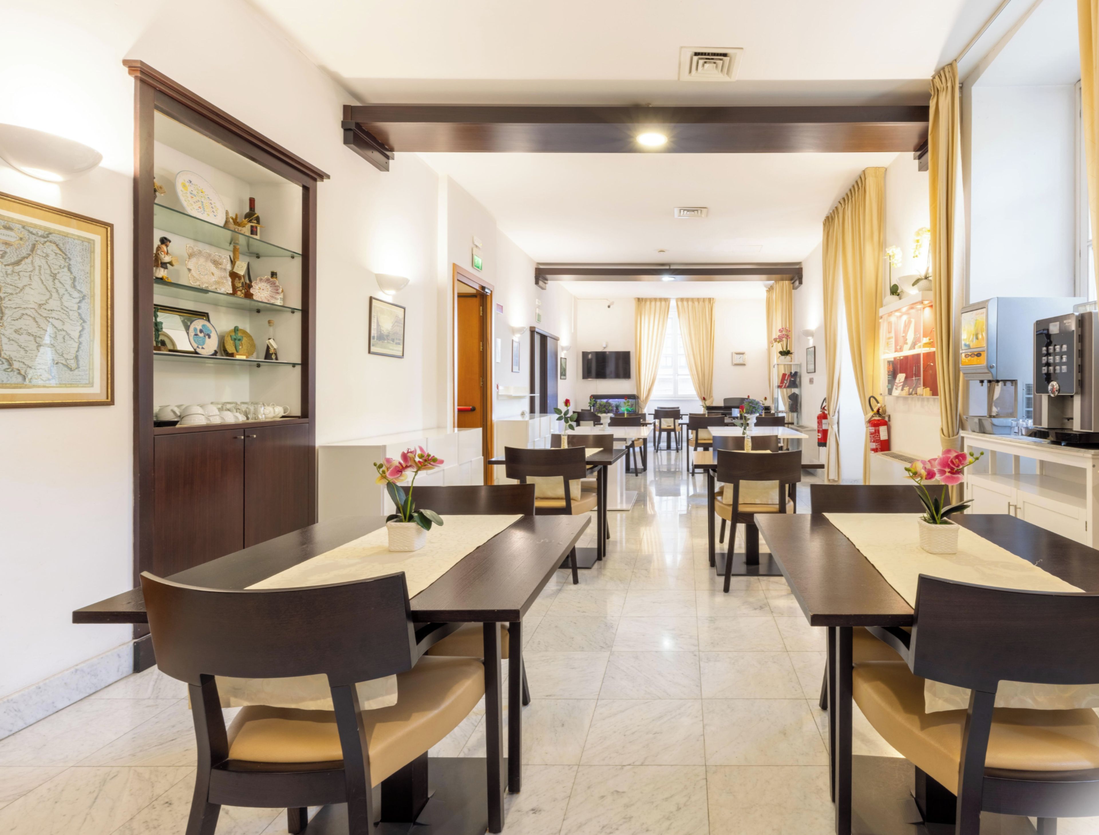 Um espaço de refeições de hotel com várias mesas e cadeiras, uma cozinha ao fundo e um mapa na parede.