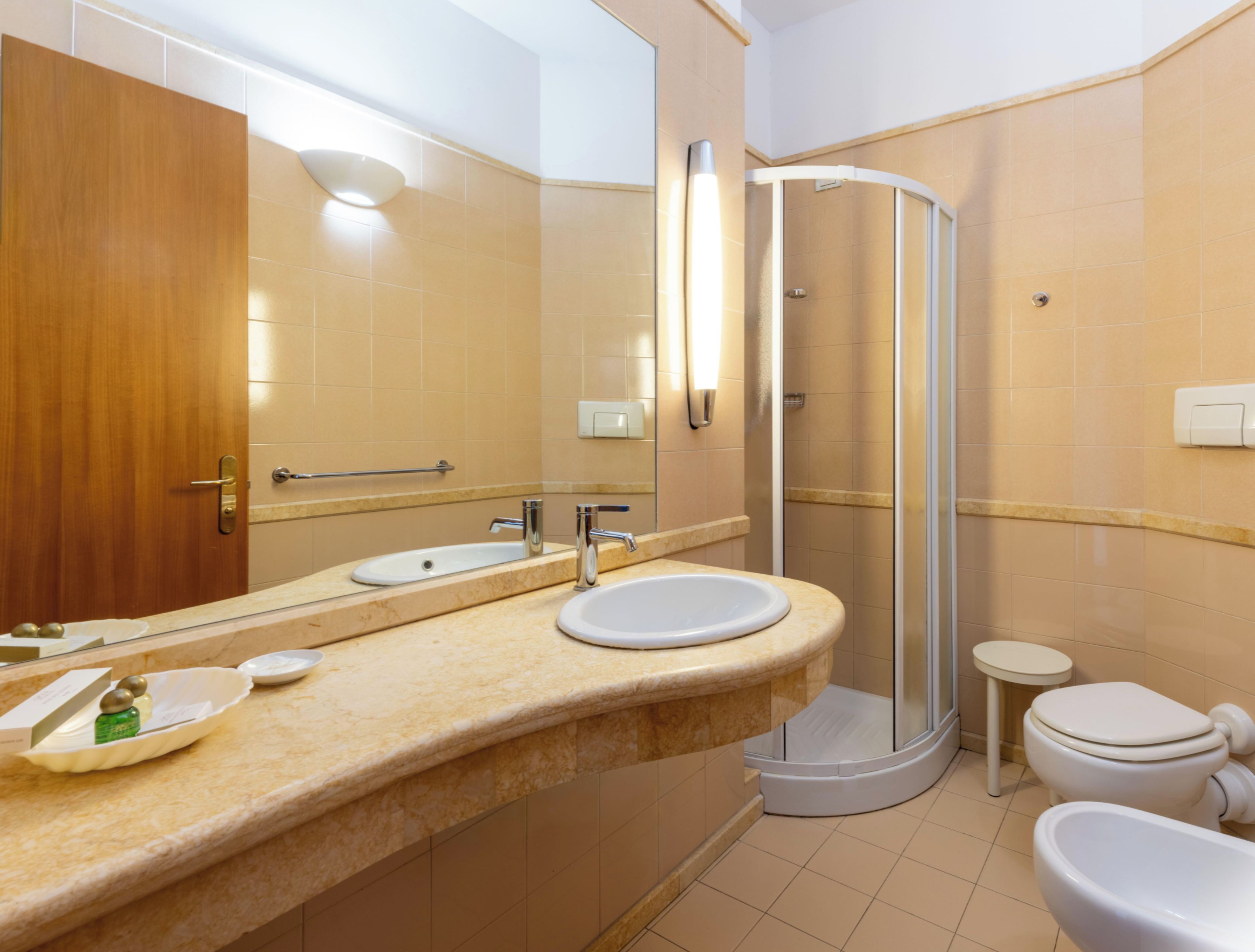 Un baño con tocador doble lavamanos, ducha con cerramiento de vidrio y un inodoro.