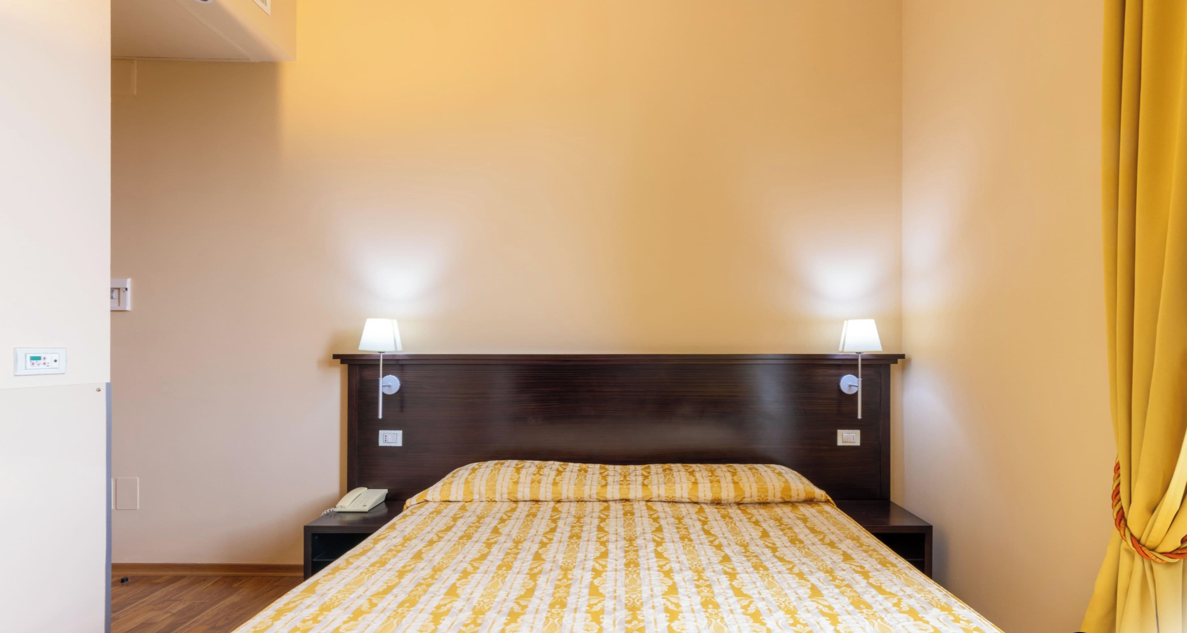 Una habitación de hotel con cama, lámparas de noche, teléfono y cortina.