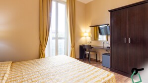 Ein Hotelzimmer mit Bett, Schreibtisch, Stuhl, Kleiderschrank und einem Fenster mit Vorhängen.