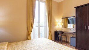 Une chambre d’hôtel comprenant un lit, un bureau, une chaise, une armoire et une fenêtre avec des rideaux.