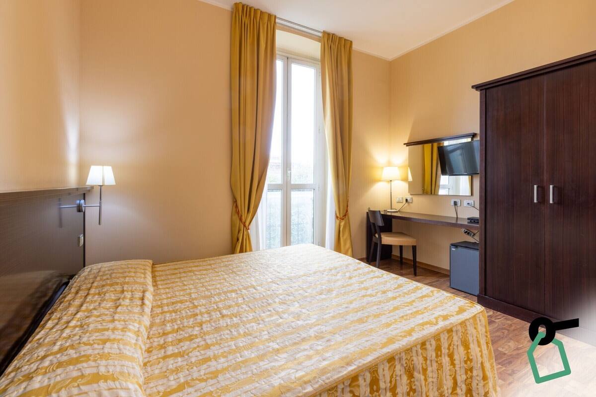 A hotel room with a bed, a desk, a chair, a wardrobe, and a window with curtains.