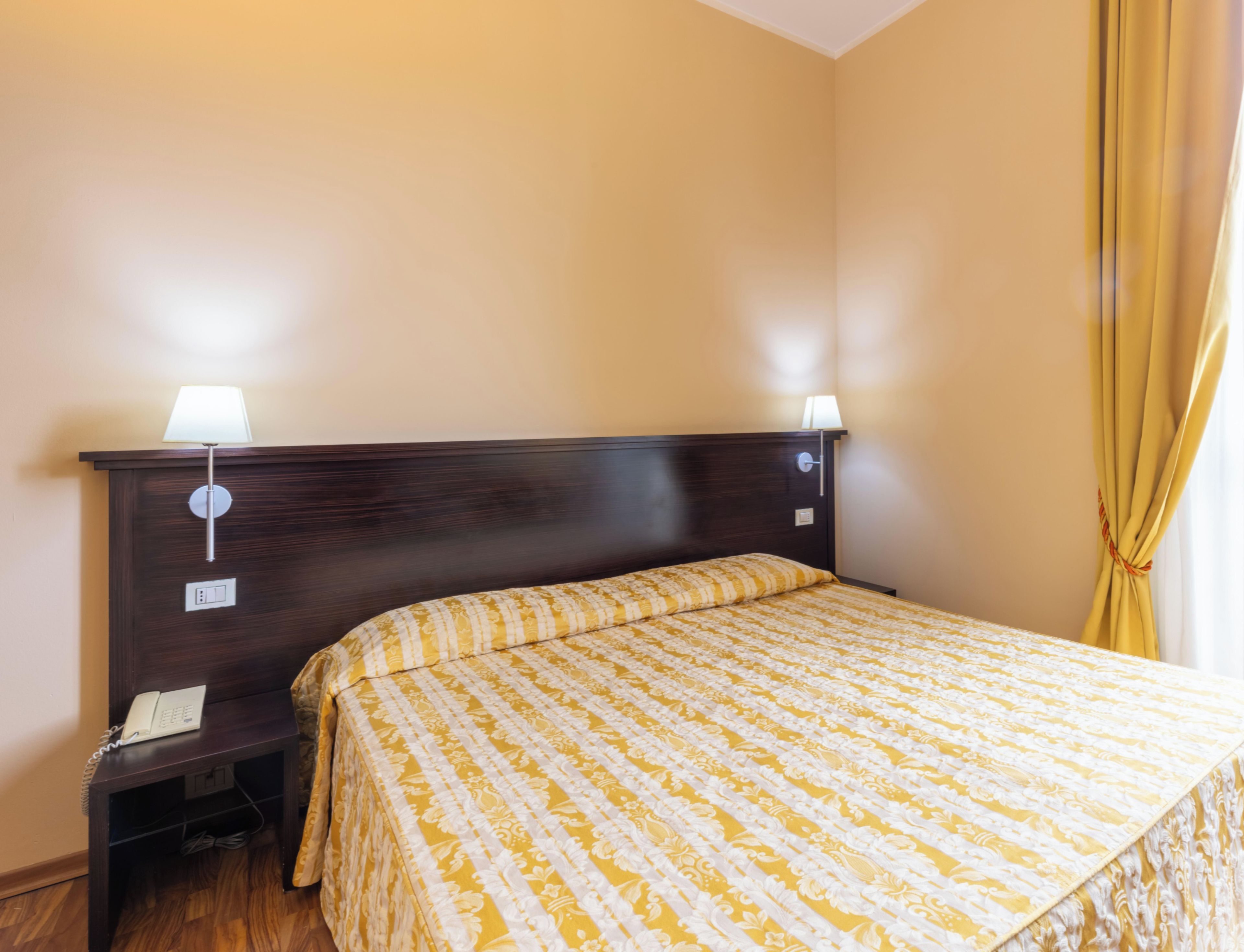 A hotel room with a bed, two bedside lamps, a telephone, and a curtain.