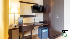 Ein Hotelzimmer mit Schreibtisch, Stuhl, Fernseher, Kleiderschrank und einem kleinen Schrank.