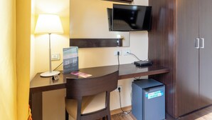 Une chambre d’hôtel équipée d’un bureau, d’une chaise, d’une télévision, d’une armoire et d’un petit meuble de rangement.