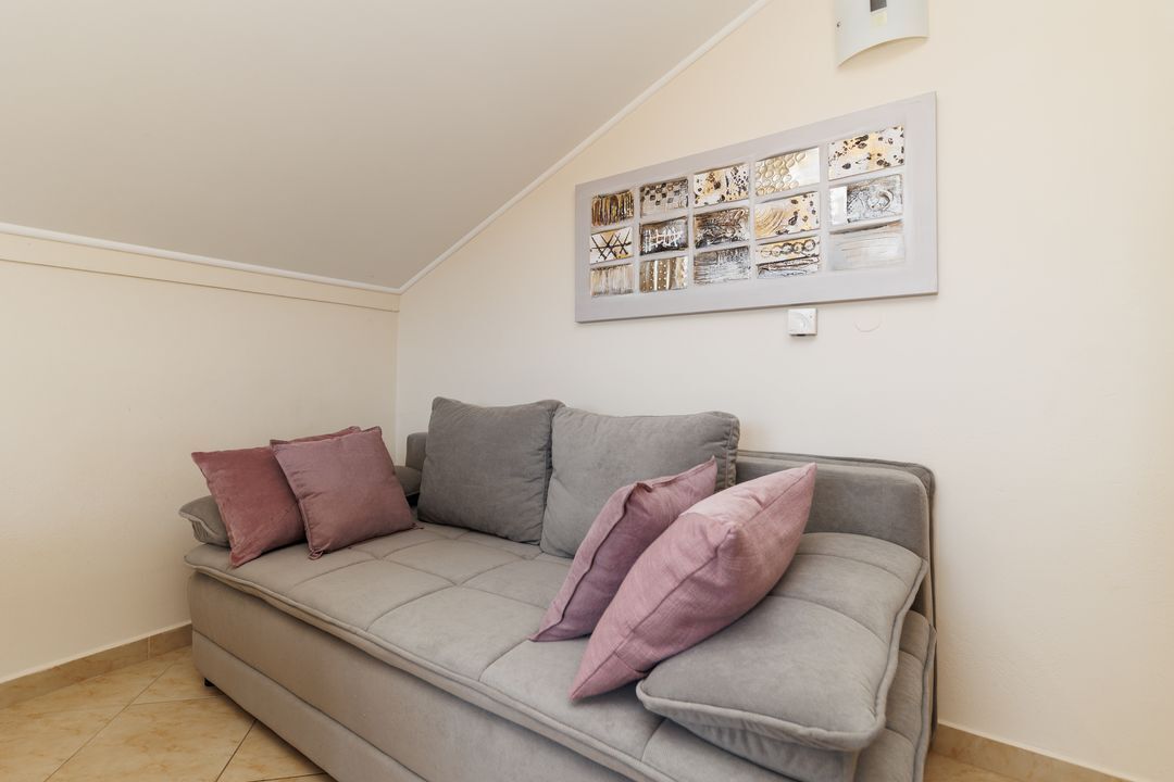 A grey sofa with multiple cushions in a room with a tiled floor and a wall-mounted artwork.