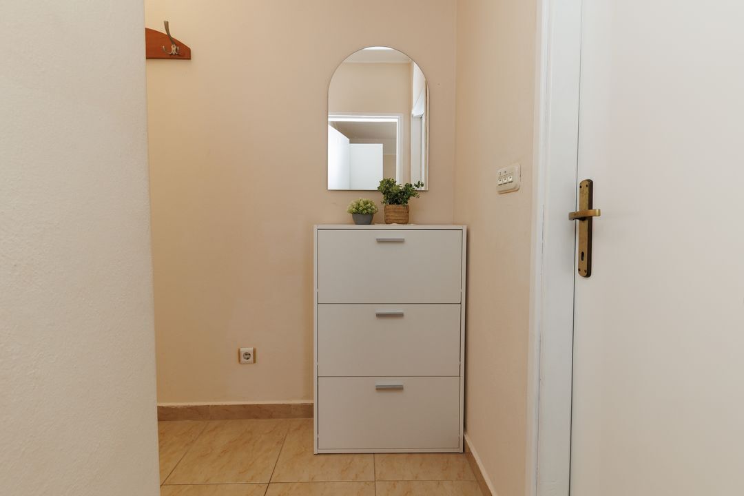 A hallway with a white cabinet, a mirror, and a door.