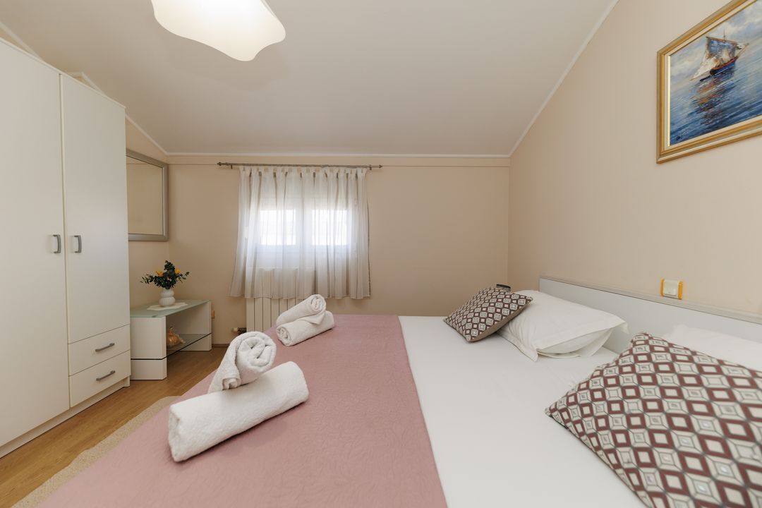 A hotel room with a bed, a bedside table, a mirror, a window with curtains, and a painting on the wall.