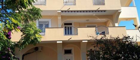A two-story building with a flat roof, balconies, and a central entrance.