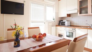 Egy modern konyha fehér szekrényekkel, mikrohullámú sütővel, hagyományos sütővel és egy falra szerelt, síkképernyős televízióval.