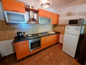 A kitchen with orange cabinets, a gas stove, a microwave, and a refrigerator. - Apartment Andrea (Novi Vinodolski)