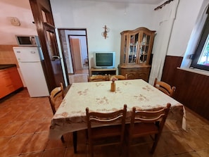 A dining area with a table set for six, a wooden cabinet with glass doors, a television, and a refrigerator. - Apartment Andrea (Novi Vinodolski)