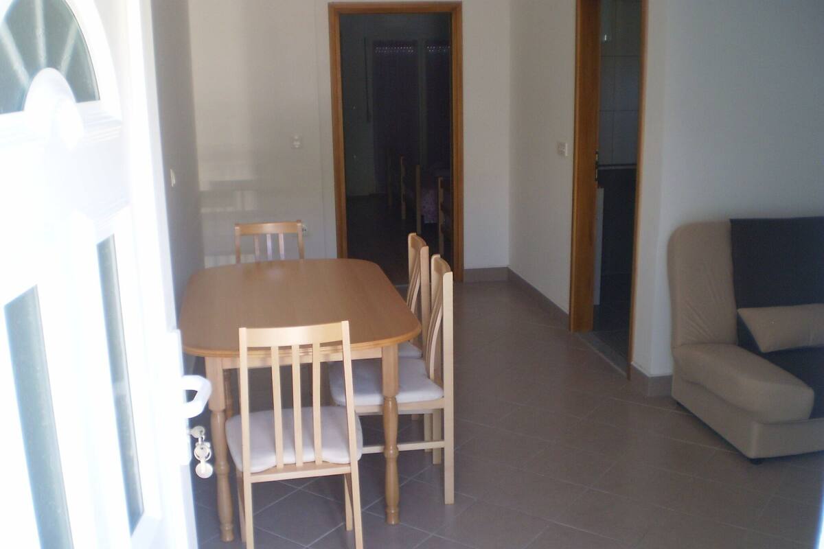 A dining area with a wooden table and chairs, a sofa, and a tiled floor.