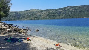 A pebble beach with clear water, a boat in the distance, and a hilly landscape in the background. - Apartments Gunja (Marina)