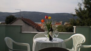A terrace with a table set for two, overlooking a scenic view of hills and buildings. - Apartments Gunja (Marina)