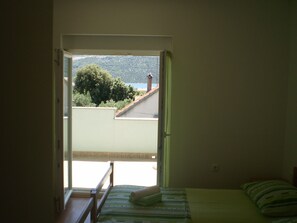Ein Schlafzimmer mit einem Bett, einem Fenster und Blick auf einen Baum und ein Gebäude.