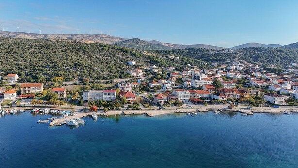 A coastal town with residential buildings, a marina with boats, and wind turbines in the background. - Apartments Gunja (Marina)