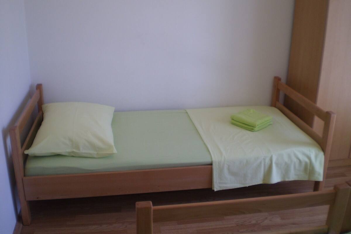 A small, single-bed room with a wooden frame and a light green mattress.