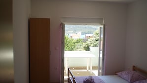 A bedroom with a bed, a wooden chair, a table, and a view of the outdoors. - Apartments Gunja (Marina)
