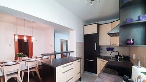 A modern kitchen with a dining area, featuring a central island, dark cabinetry, and a tiled backsplash. - Apartment Frano (Crikvenica)