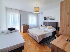 A hotel room with a bed, a desk, a dresser, and a window with sheer curtains. - Apartment Frano (Crikvenica)