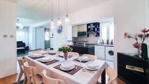 A dining area with a table set for six, chairs, a vase with flowers, and a kitchen in the background. - Apartment Frano (Crikvenica)