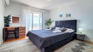 A bedroom with a bed, a desk, a chair, a lamp, and a view of the outdoors. - Apartment Frano (Crikvenica)