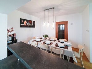 A dining area with a long table set for four, white chairs, and a dark countertop. - Apartment Frano (Crikvenica)