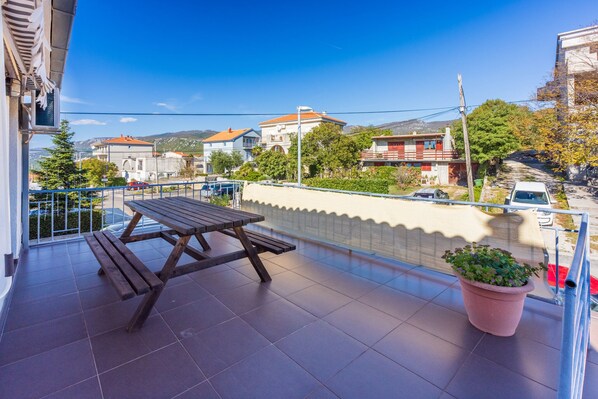 A balcony with a wooden table and a potted plant, overlooking a residential street with houses and a clear blue sky. - House Sunshine (Novi Vinodolski)