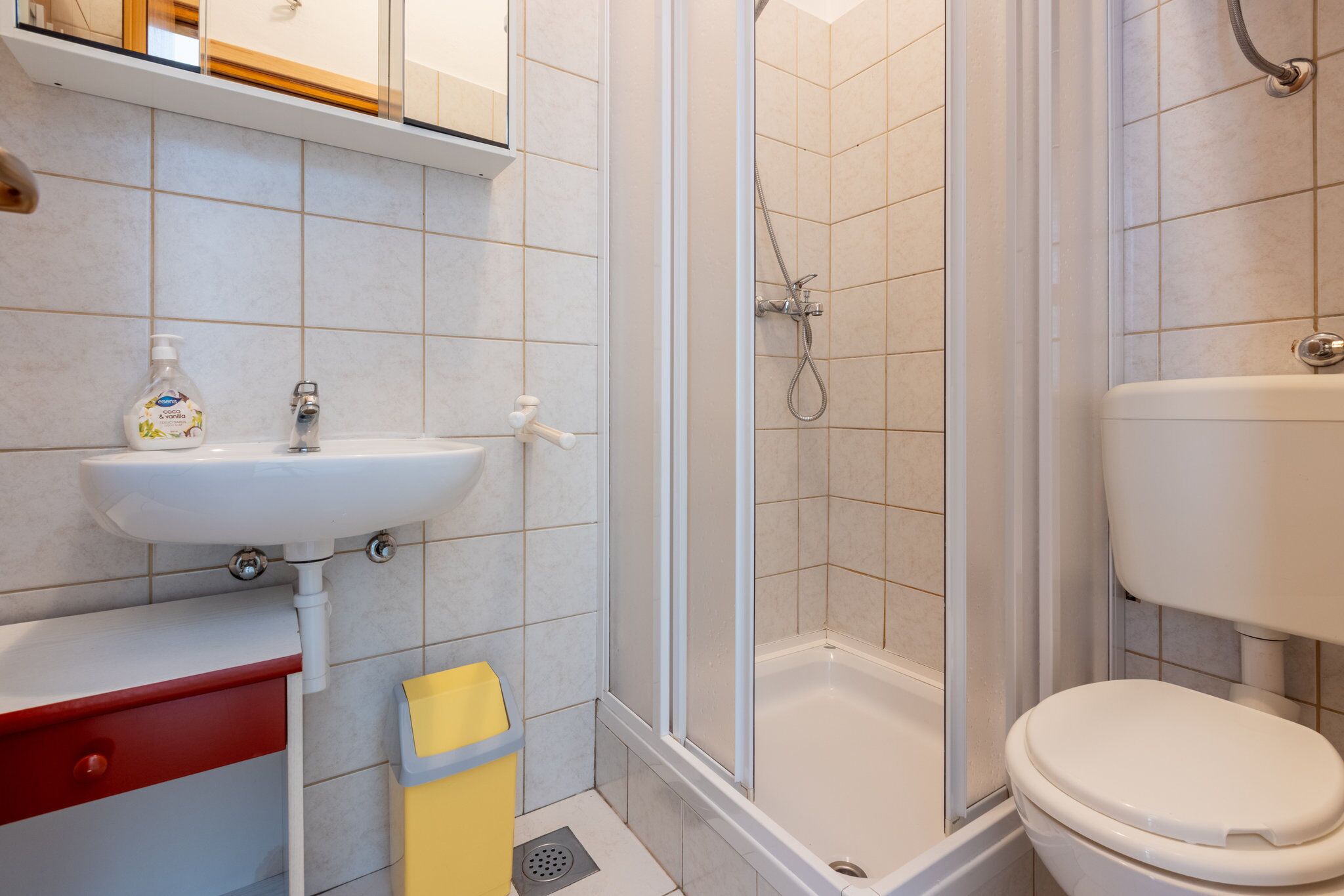 A bathroom with a sink, toilet, shower, and a yellow trash bin.