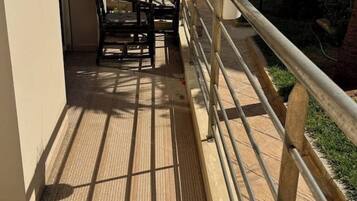 Um deck de madeira com guarda-corpo de metal, uma cadeira e uma mesa.