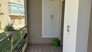 Un balcón con barandilla de metal, un armario blanco y un bote de basura verde.