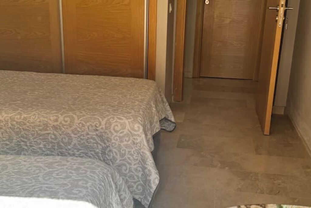 Un dormitori amb un llit cobert per un estovat estampat, portes d'armari de fusta i un terra de rajoles.