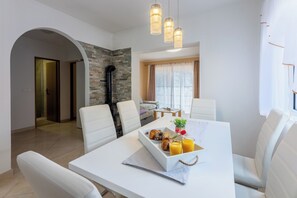 A modern dining area with a white table, four white chairs, and a breakfast tray with croissants and orange juice. - Apartments Natalija (Novi Vinodolski)