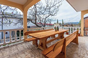 A wooden table and benches on a stone-tiled patio with a white balustrade. - Apartments Natalija (Novi Vinodolski)