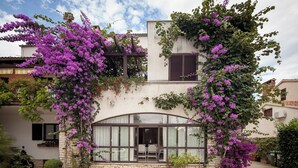 Uma casa de dois andares com fachada de pedra, uma grande janela em arco e trepadeiras roxas com flores.