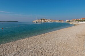 Una playa de guijarros con una vista despejada de un pueblo costero y una isla distante.