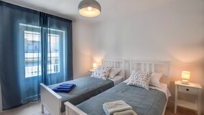 Una camera da letto con due letti, un'ampia finestra con tende, lampade da comodino e un lampadario.